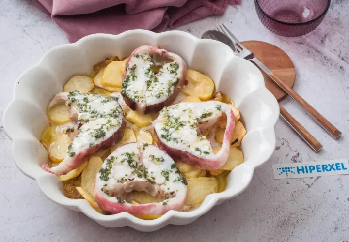 Rodajas de pescado rosado al horno con patatas, cubiertas de hierbas frescas.