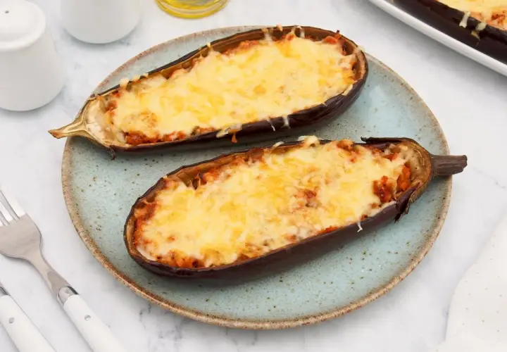 Dos mitades de berenjenas rellenas de atún, gratinadas con queso derretido, servidas en un plato azul.