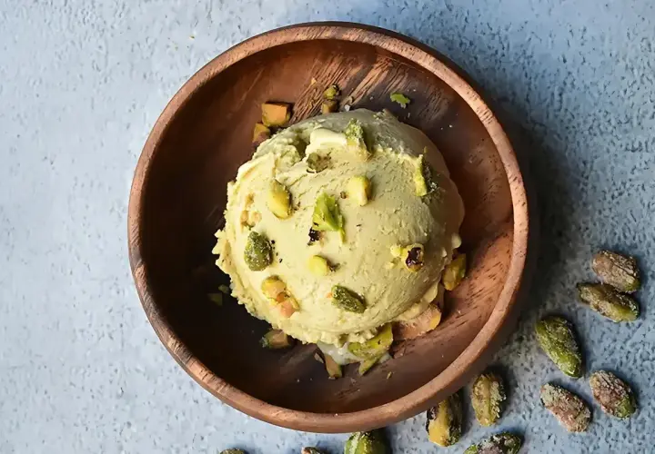Cremoso helado de pistacho, adornado con trozos de pistacho, servido en un cuenco de madera rústico.