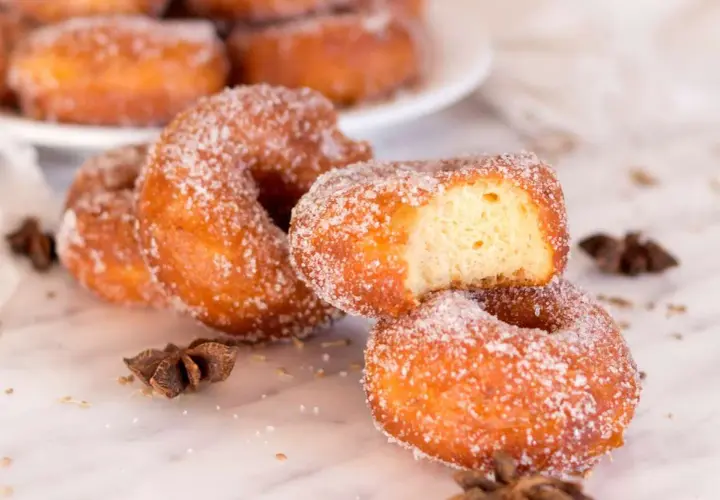 Rosquillas de carnaval espolvoreadas con azúcar, una con un mordisco, junto a anís estrellado.