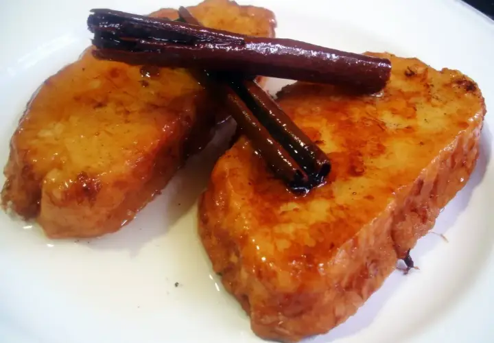Dos deliciosas torrijas de vino, doradas y bañadas en almíbar, coronadas con canela en rama.