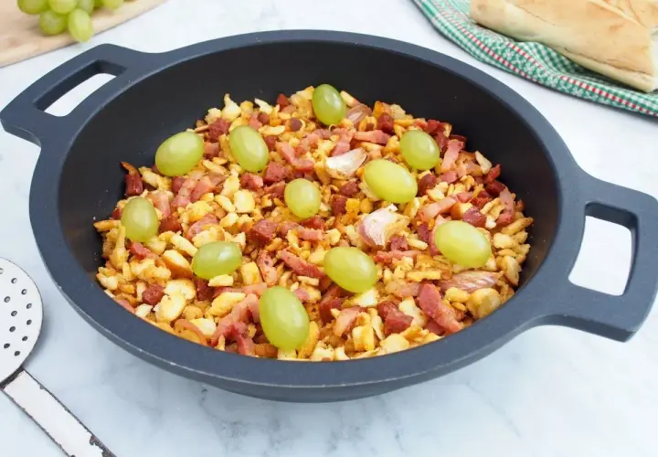 Migas manchegas con uvas verdes y ajos en una sartén. Un plato tradicional listo para disfrutar.