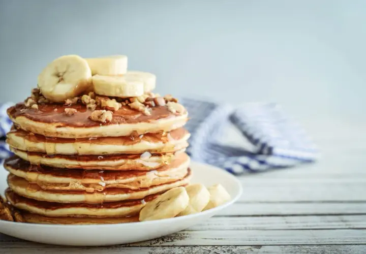 Una pila de tortitas de plátano cubiertas de miel y nueces, con rodajas de plátano fresco encima.