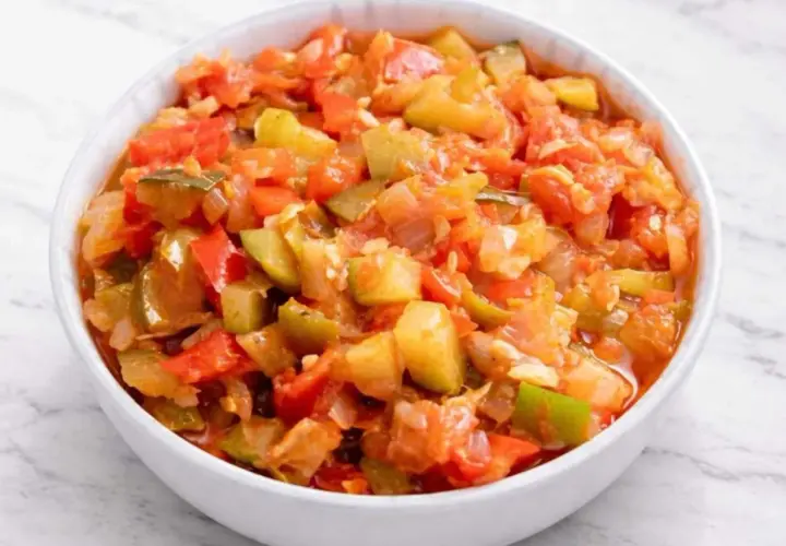 Un tazón blanco lleno de pisto manchego, un guiso vibrante de verduras picadas como tomate, pimiento y calabacín.