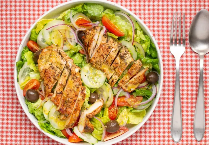 Deliciosa ensalada de pollo a la parrilla con lechuga, tomate, pepino, cebolla morada y aceitunas.