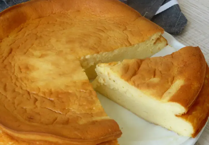 Tarta de queso Philadelphia dorada y esponjosa, con una porción cortada que revela su interior cremoso.