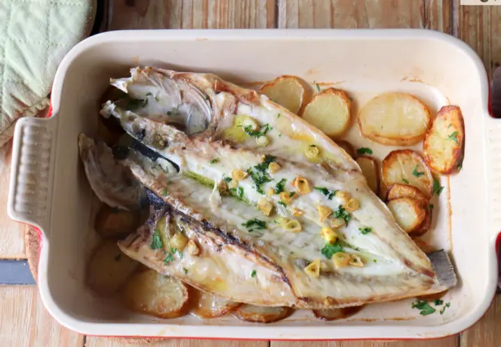 Lubina a la espalda horneada con patatas y ajo, lista para servir.