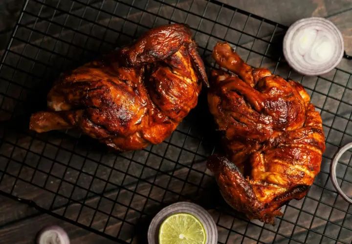 Dos jugosos pollos a la brasa, dorados y listos para disfrutar, acompañados de rodajas de cebolla roja y limón.