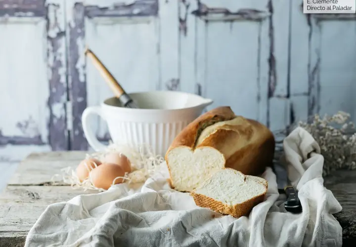Pan brioche para torrijas, huevos y batidor sobre mesa rústica.