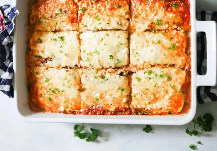 Una deliciosa lasaña de berenjena recién horneada, cubierta de queso derretido y perejil picado, lista para servir.