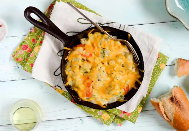 Coliflor gratinada burbujeante en sartén de hierro fundido, lista para disfrutar con pan crujiente.