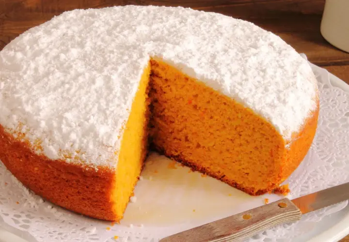 Pastel de zanahoria esponjoso, cubierto de azúcar glas, con una rebanada retirada.