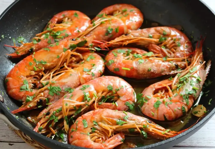Gambones al ajillo chisporroteando en una sartén, con perejil fresco espolvoreado. ¡Un plato delicioso!