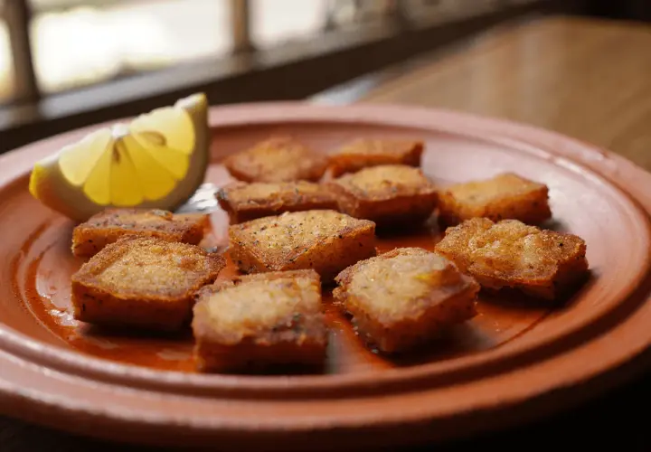 Deliciosos trozos de bacalao rebozado, dorados y crujientes, servidos en un plato de barro con una rodaja de limón.