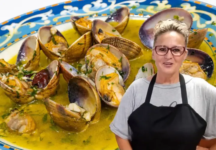 Una mujer sonriente presenta un plato de almejas al ajillo, conchas abiertas en una salsa dorada con perejil picado.