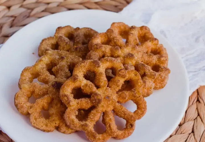 Un plato blanco con varios buñuelos de viento espolvoreados con canela y azúcar.
