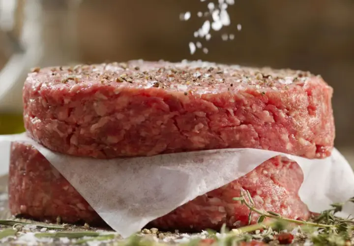Dos hamburguesas de carne picada apiladas, sazonadas con sal y pimienta.
