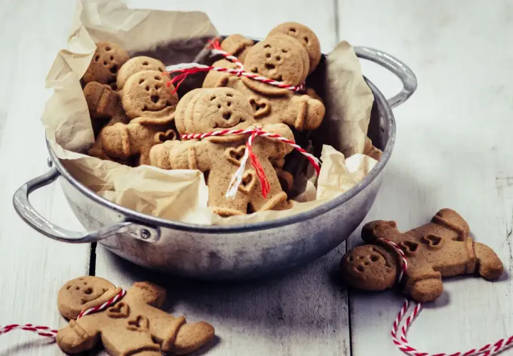 Un cuenco lleno de galletas de jengibre con forma de hombrecito, algunas atadas con hilo rojo y blanco.