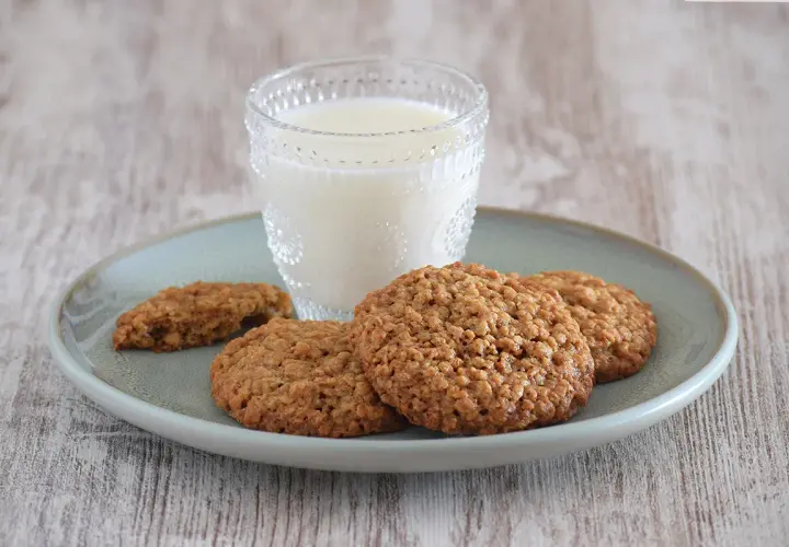 Un vaso de leche acompaña a unas deliciosas galletas de avena sobre un plato.