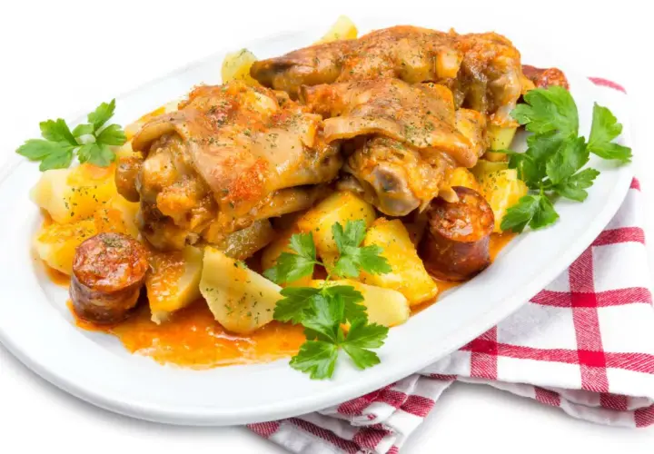 Manitas de cerdo guisadas con patatas y chorizo, decoradas con perejil fresco. Un plato tradicional y sabroso.