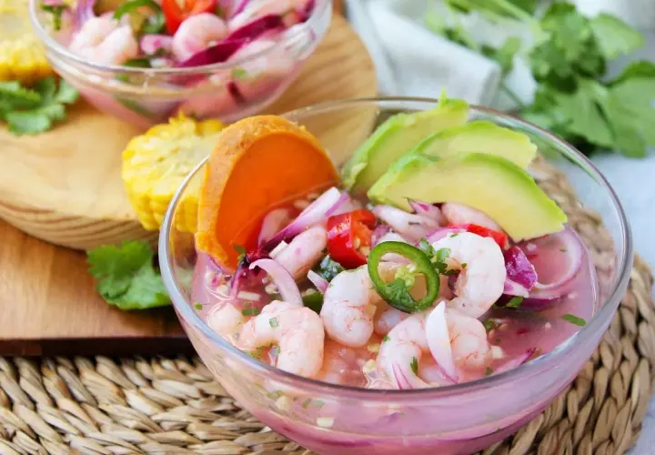 Delicioso ceviche de gambas con aguacate, cebolla morada, chile jalapeño y tomate. Servido en un cuenco de cristal, acompañado de maíz y cilantro fresco.