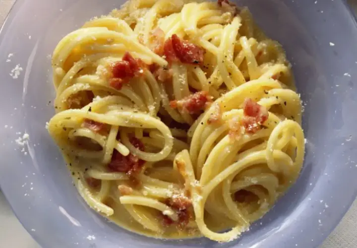 Un plato de pasta carbonara cremoso con trozos de panceta crujiente y espolvoreado con queso rallado.