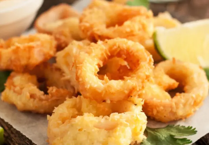 Crujientes calamars a la romana, dorados y listos para disfrutar, acompañados de gajos de limón y perejil fresco.