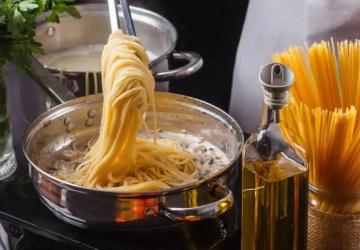 Unos espaguetis se añaden a una sartén con salsa cremosa, listos para convertirse en una deliciosa pasta al ajillo.