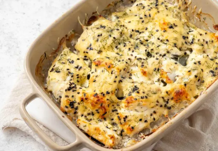 Bacalao a la nata gratinado, cubierto con semillas negras y eneldo, burbujeando en una fuente de cerámica.