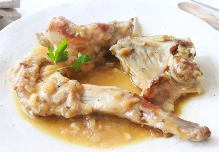 Deliciosas recetas de conejo guisado en salsa, servido en plato blanco con perejil fresco.