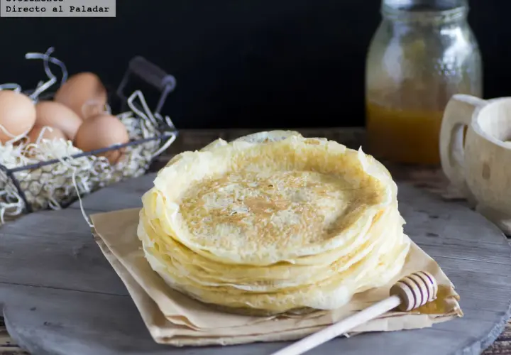 Pila de filloas gallegas recién hechas, con miel en un tarro y huevos en una cesta al fondo.