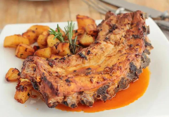 Costillas al horno con patatas doradas y romero fresco. Un plato jugoso y apetitoso.
