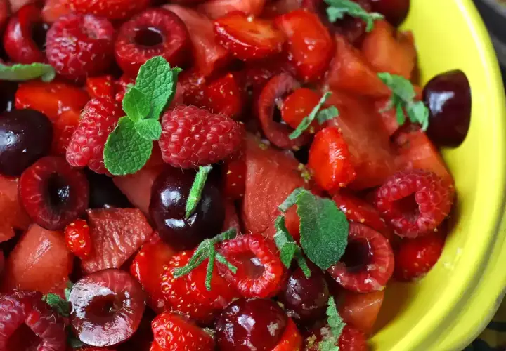 Delicioso postre con fresas, frambuesas, cerezas y menta en un tazón amarillo.