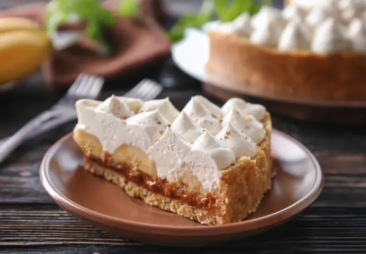 Rebanada de tarta banoffee con plátano, dulce de leche y crema batida, espolvoreada con canela.