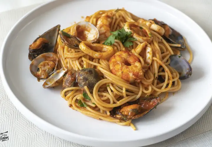 Espaguetis a la marinera con gambas, mejillones, almejas y calamares, servidos en un plato blanco.
