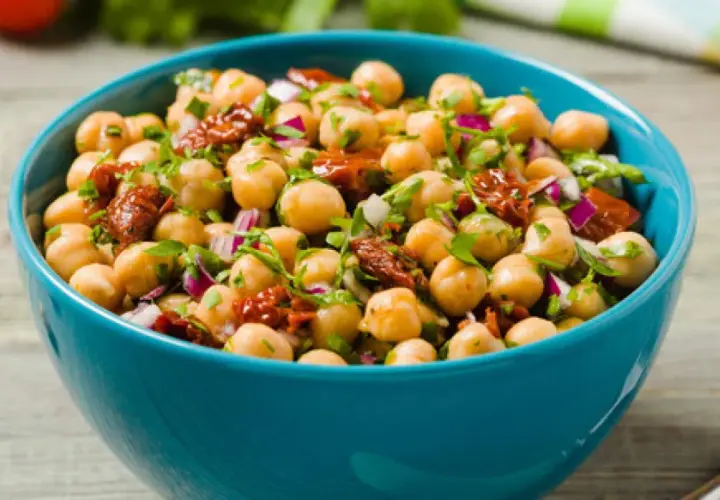 Ensalada de garbanzos fresca y colorida con tomate seco y cebolla morada en un cuenco azul.