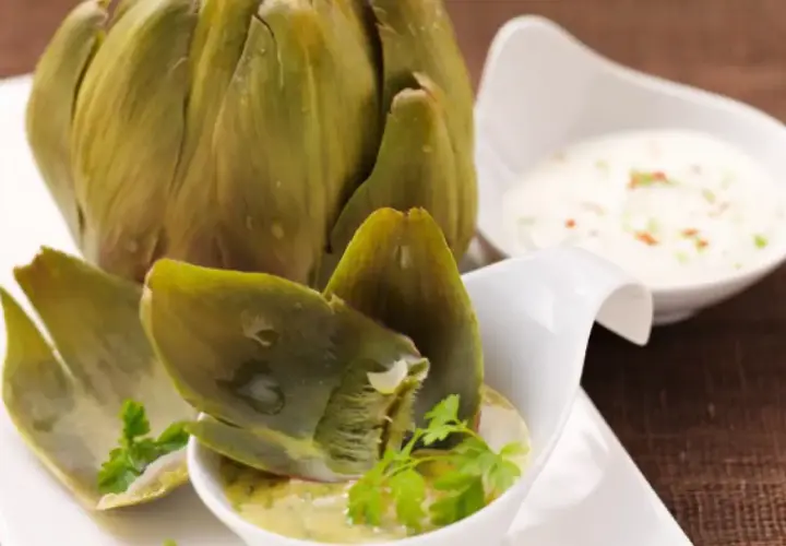 Alcachofas enteras cocidas, servidas con salsas para mojar. Una delicia para disfrutar.