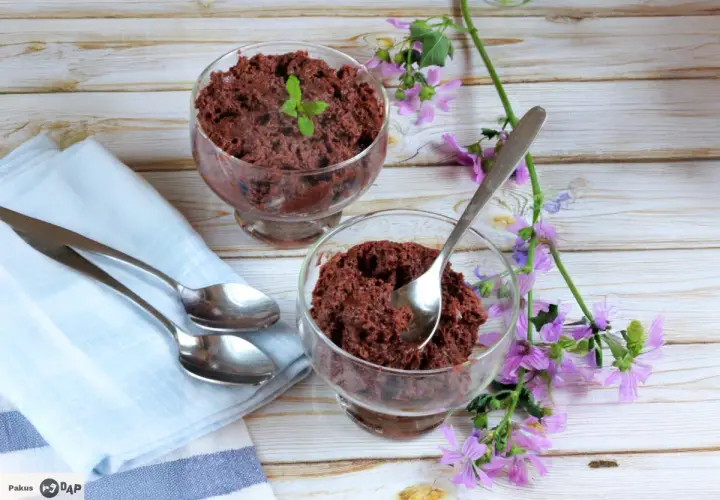 Dos copas de delicioso mousse de chocolate, decoradas con menta y flores moradas, listas para disfrutar.