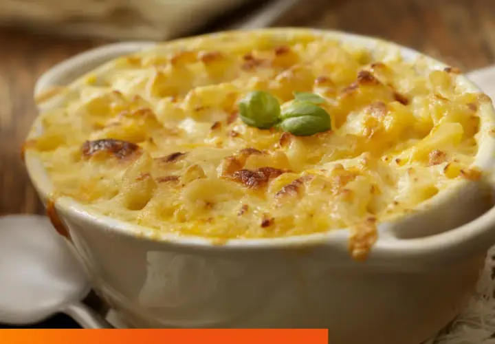 Un plato cremoso de macarrones con queso, gratinado y decorado con una hoja de albahaca.