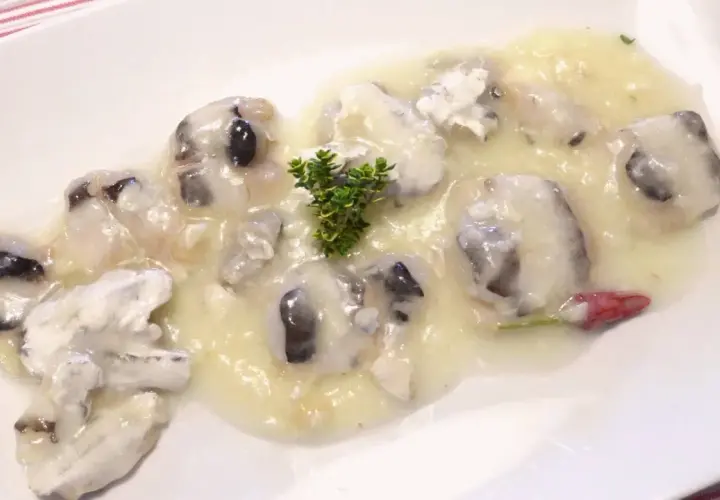 Deliciosas cocochas de merluza en salsa cremosa, adornadas con una ramita de tomillo y un toque de pimiento rojo.