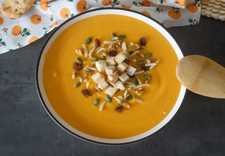 Un cremoso puré de calabaza adornado con picatostes, nueces, pasas y semillas de calabaza.