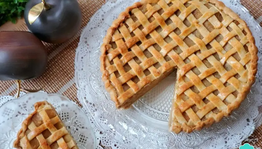 Tarta de manzana de la abuela, dorada y con un enrejado perfecto. Un trozo ya servido en un plato de cristal.