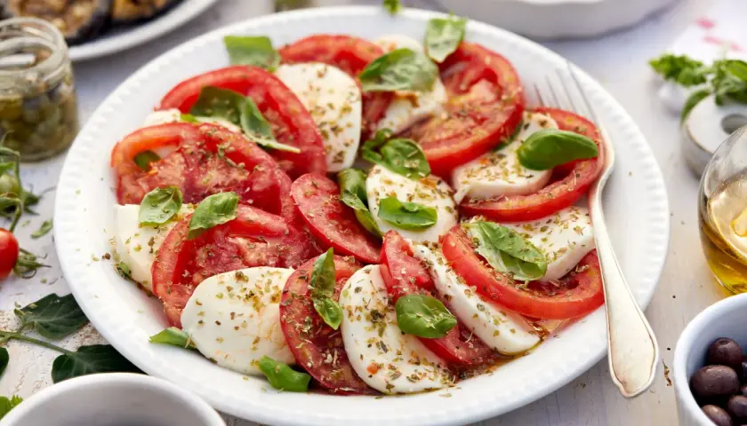 Ensalada caprese fresca con rodajas de tomate y mozzarella, aderezada con albahaca y especias.