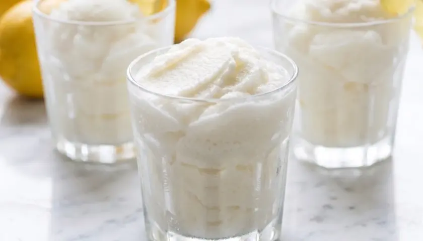 Tres vasos de sorbete de limón refrescante, con limones amarillos y hojas de menta al fondo.