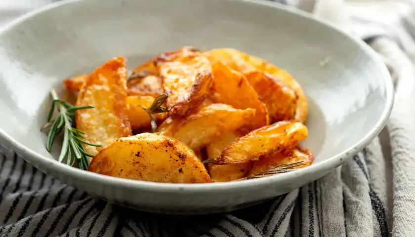 Patatas al horno en rodajas, doradas y crujientes, servidas en un cuenco con romero fresco.