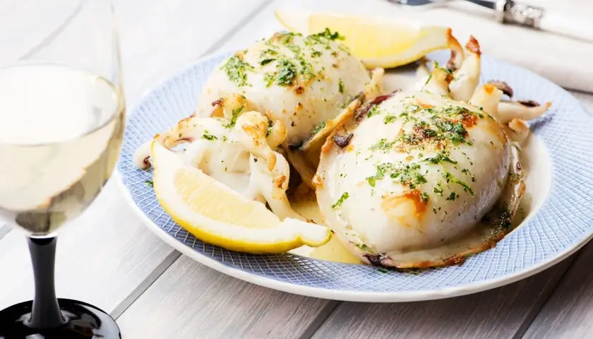 Delicioso sepia a la plancha, servido con gajos de limón y perejil picado, acompañado de una copa de vino blanco.