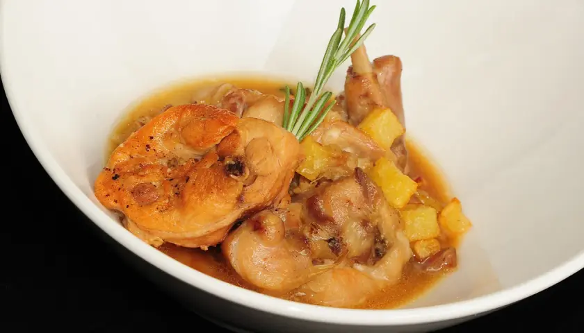 Delicioso conejo en salsa con patatas y romero, servido en un cuenco blanco.