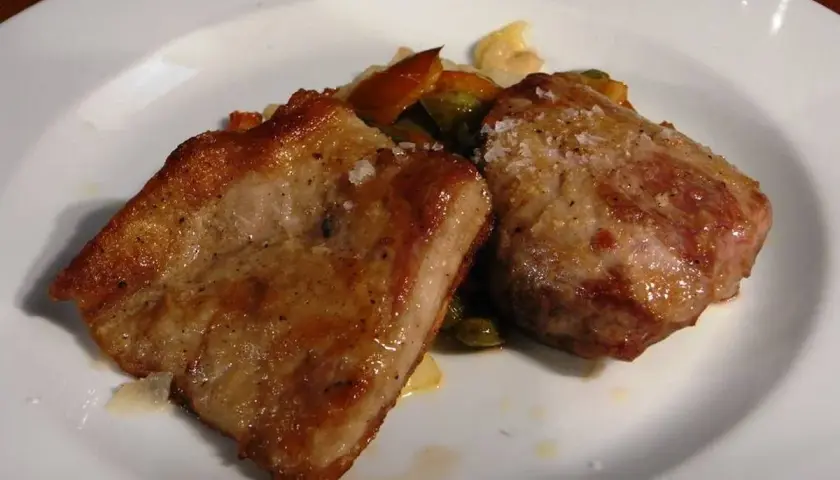 Dos trozos de secreto de cerdo a la plancha, dorados y jugosos, servidos con verduras salteadas en un plato blanco.