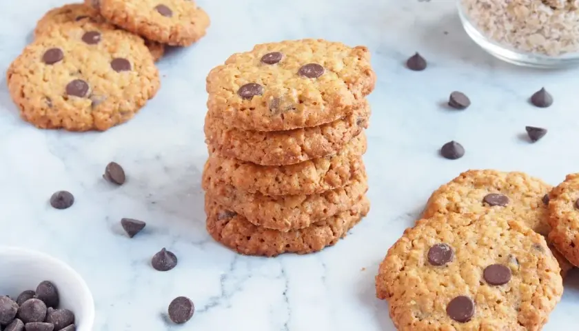 Deliciosas galletas de avena y chocolate, apiladas y esparcidas, con chispas de chocolate y avena en un frasco.