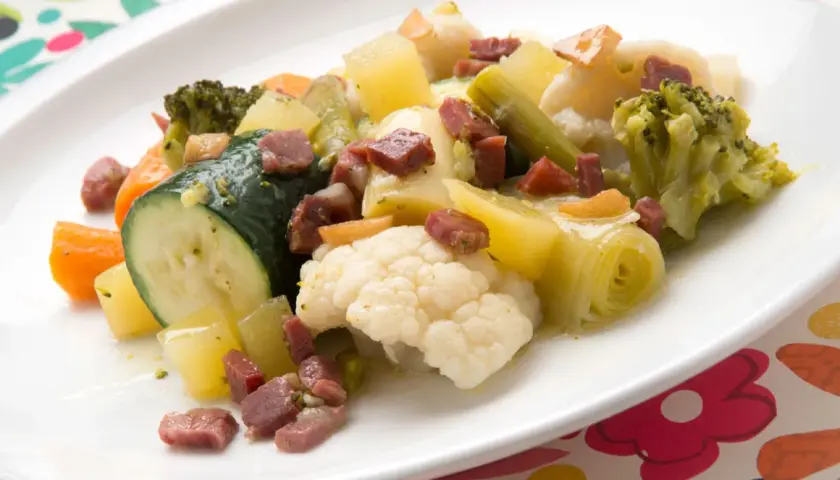 Un colorido panache de verduras con brócoli, coliflor, calabacín, zanahoria y patatas, salpicado de trocitos de jamón.